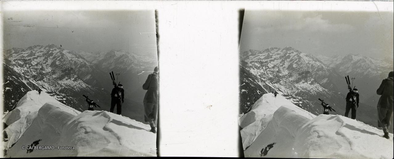 Concorrenti con gli sci a spalla sulla cima del Madonnino e sullo sfondo il Diavolo ed il Grabiasca