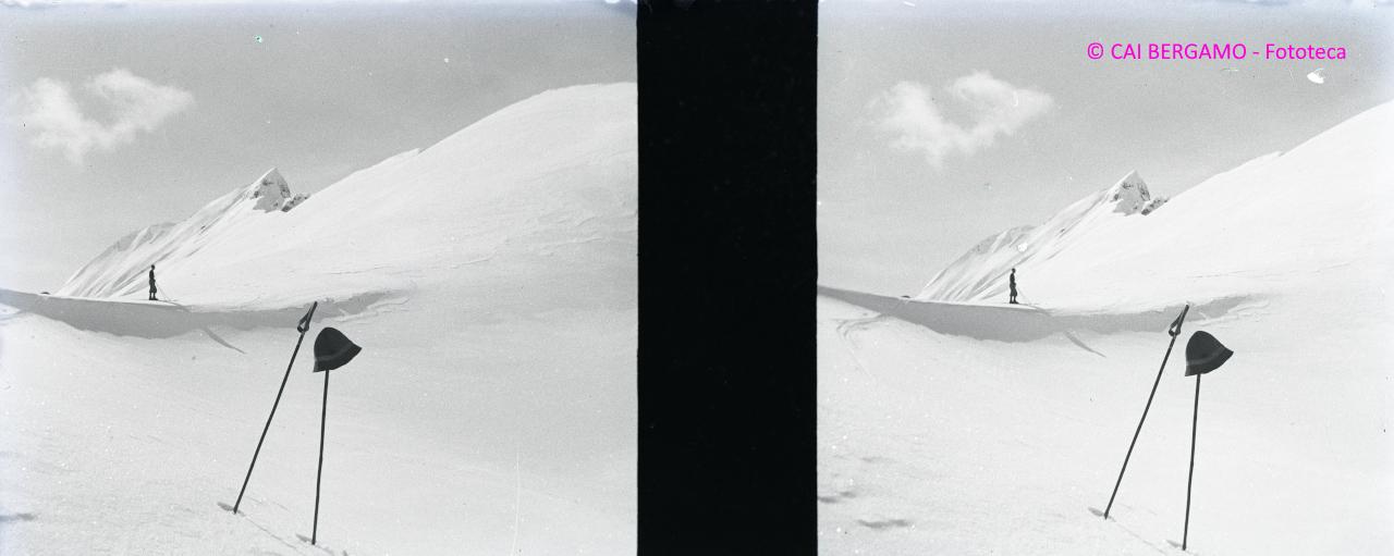 Scialpinista sullo sfondo e cappello su bastoncino in primo piano