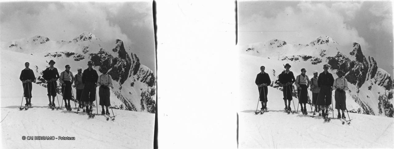 Skiatori allineati con il Pizzo Recastello sullo sfondo con la cresta dei Corni Neri sulla destra