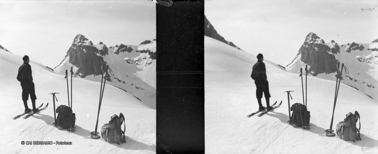 Skiatore tra bastoncini e zaini dei compagni di gita sotto lo sguardo del Poris con il passo di Valsecca